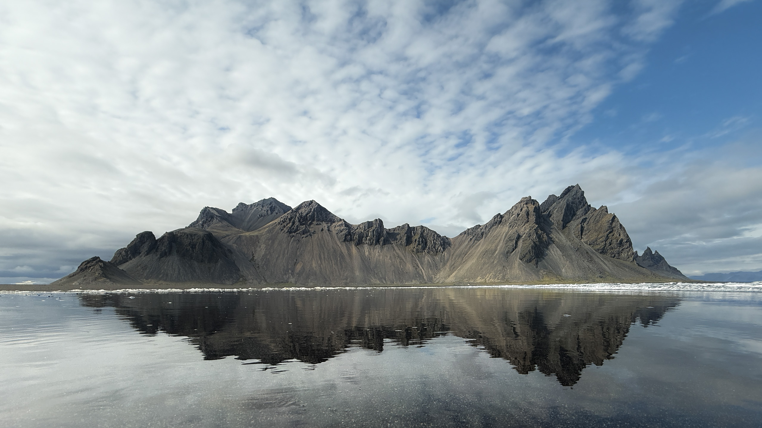 Vestrahorn mountain range mirrored in a glassy black-sand beach in Iceland